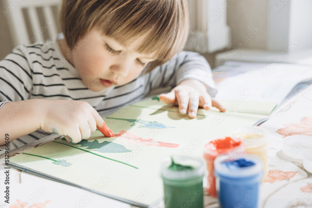 Finger painting. Portrait of cute little boy painting with fingers at home. Close-up of child's hand in colorful paints. Early education concept. Sensory play. Development of fine motor skills. Finger painting. Portrait of cute little boy painting with fingers at home. Close-up of child's hand in colorful paints. Early education concept. Sensory play. Development of fine motor skills.