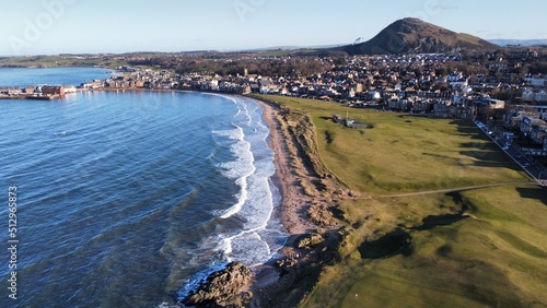 Aerial view looking out over North Berwick town and golf course with waves crashing onto the shore. North Berwick Scotland. 