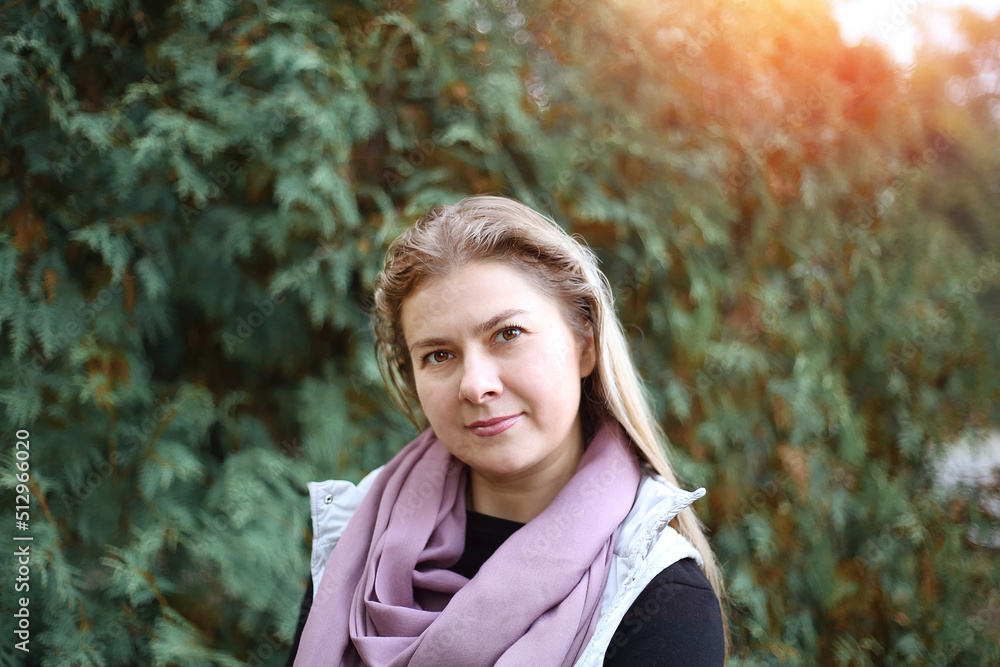 Young pretty Caucasian woman 35+ looking at the camera in a rose pink scarf. Casual clothes for walking. Green park background. Sports. Yoga. Lifestyle concept Young pretty Caucasian woman 35+ looking at the camera in a rose pink scarf. Casual clothes for walking. Green park background. Sports. Yoga. Lifestyle concept