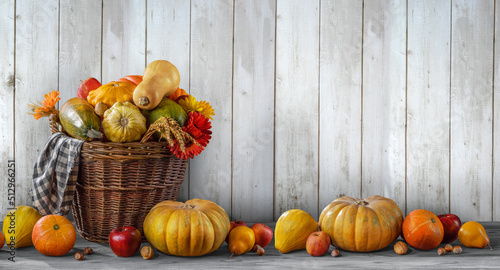 Fototapeta Naklejka Na Ścianę i Meble -  Thanksgiving day background with empty copy space. Pumpkin harvest in wicker basket. Squash, orange vegetable autumn fruit, apples, and nuts on a wooden table. Halloween decoration fall design