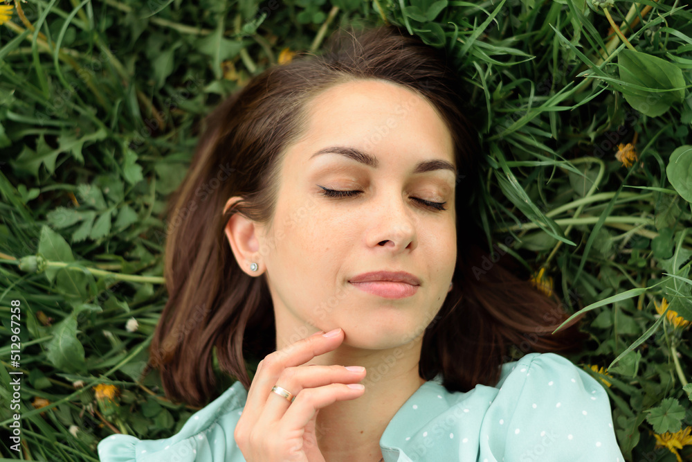 Naklejka premium Portrait of a beautiful happy young woman with her eyes closed, lying on the grass on a summer day, top view.Mental health,closeness to nature,summer concept.
