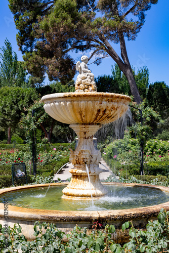 Font. Park. Roses. Stone fountain next to a park full of green vegetation and a variety of flowers of different colors in the city of Madrid, in Spain. Europe. Vertical photography. photo