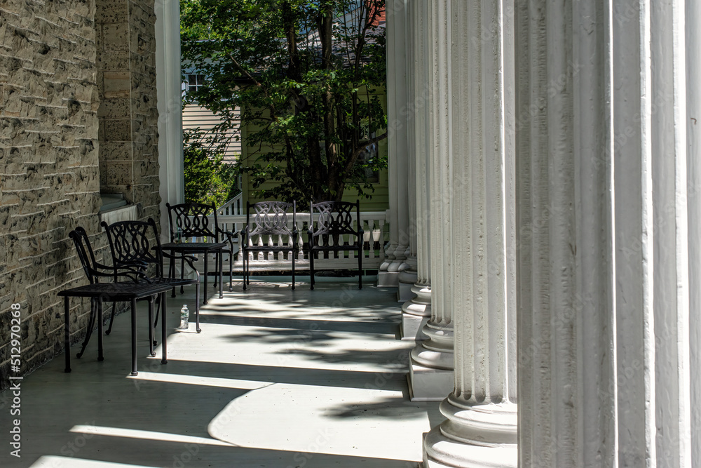 Metal chairs and a table on a porch.  White pillars adorn this very large porch located in Cooperstown, NY.