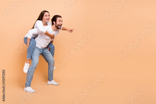 Full size photo of funky young brunette couple hug index empty space wear shirt jeans sneakers isolated on beige background