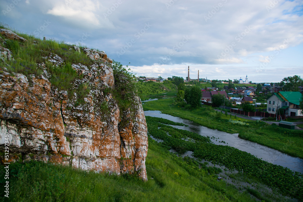 a rock near the river and the village against the background of the sunset sky.