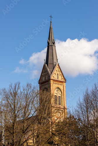 Spire of Torņakalns Church, Riga, Latvia. Vertical photo of Lutheran basilica white cloud and blue sky background. European cathedral steeple in sun. 