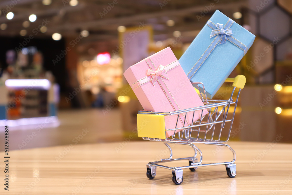 Trolley with gift boxes placed inside against a blurry background in a shopping concept.