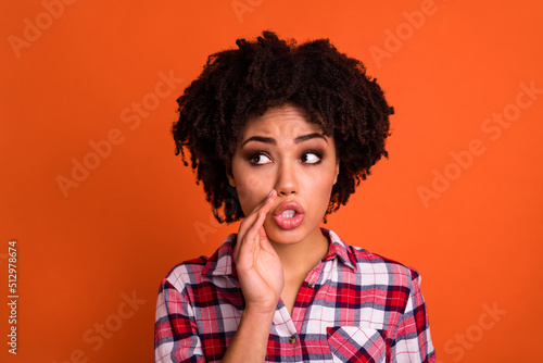 Photo of young nervous person hand near mouth tell look empty space isolated on orange color background