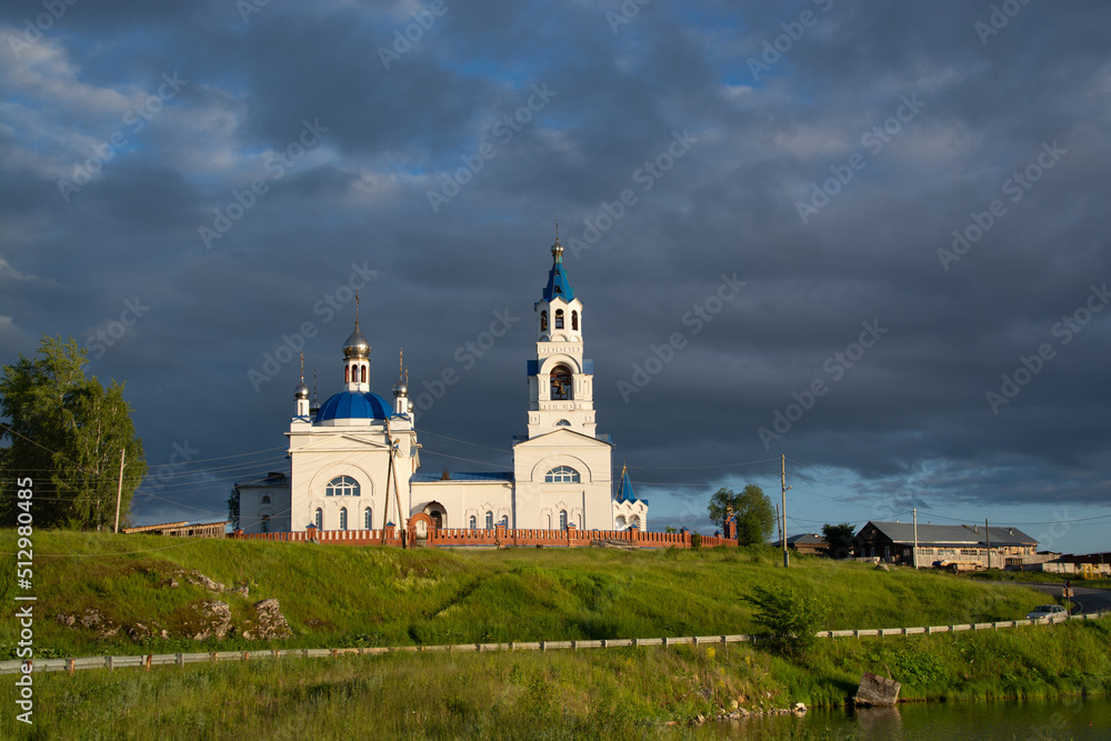 an old Orthodox church and a village on the river bank.sunset sun and black clouds.