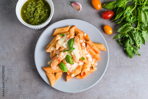 Penne pasta with tomato sauce and pesto with basil, cheese, garlic and tomatoes on a gray background.