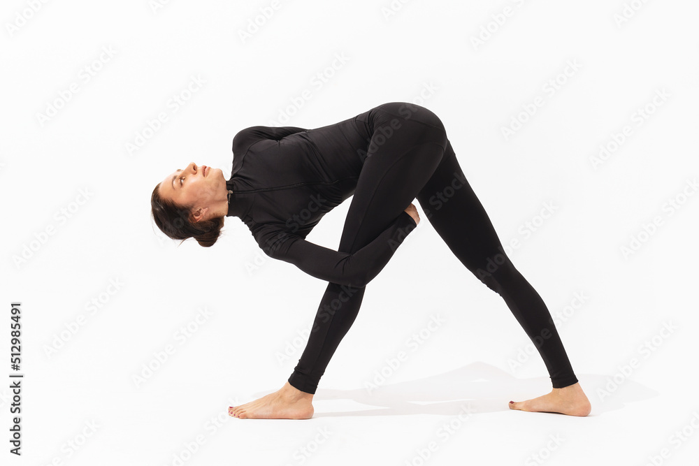 A woman in black sportswear practicing yoga performs the Trikanasana exercise, triangle pose with a hip grip on a white background