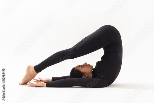 Woman in black sportswear practicing yoga, performs a variation of the Halasana exercise, plow pose on a white background photo