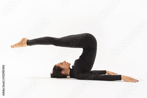 Woman in black sportswear practicing yoga doing Halasana exercise, plow pose on white background photo