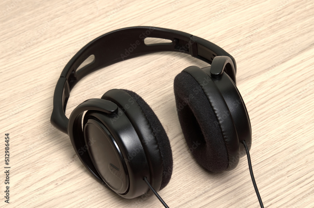 Black headphones with cable are on the wooden table Black headphones with cable are on the wooden table