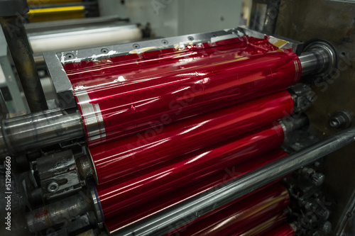 Magenta ink in the paint system compartment of a modern flexographic printing press in a print shop. Red paint in the ink feeder on the printing cylinder. Selective focus