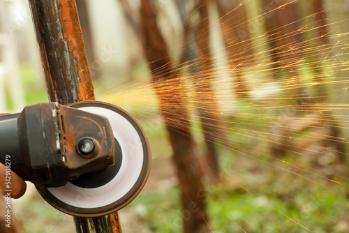 Close up of an angle grinder machine in motion, removing rust from an old metal construction outdoors with sparks flying