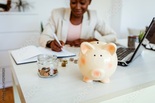 Tableau sur toile Closeup shot of coins and a piggybank on a table with an unrecognisable businesswoman working in the background