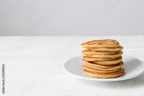 Freshly cooked pancakes on plate on white wooden table Copy space