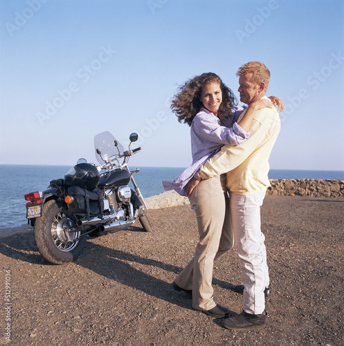 USA, California, Point Mugu, Couple hugging on coast next to motorcycle photo