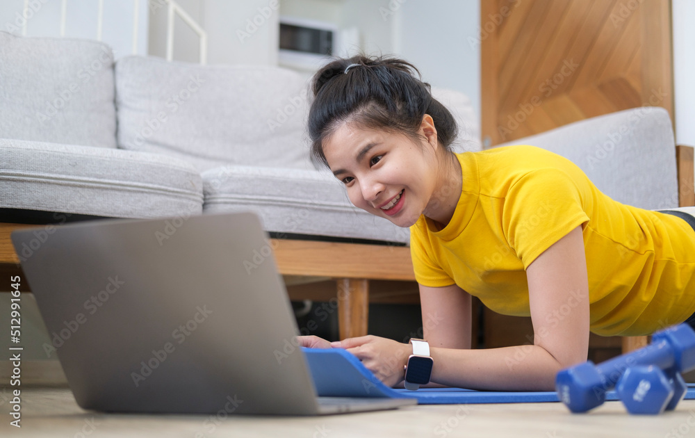 Fototapeta premium Sporty young woman using computer laptop during morning workout at home. Sport, fitness and healthy lifestyle concept.