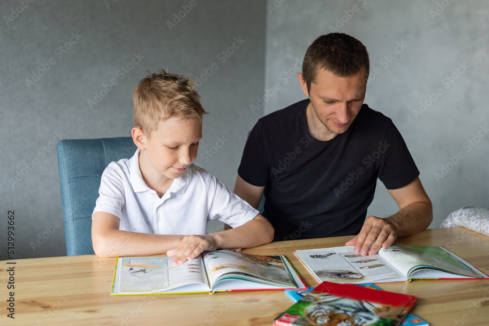 A cute boy is sitting at the table with his dad and watching a book about snakes