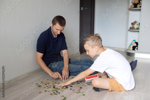 A cute boy with a cheerful dad is collecting a puzzle lying on the floor in a room