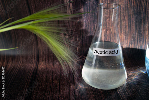 Acetic acid in a flask against the background of a wooden wall with green grass. Dietary supplement concept with place for text