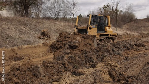 Bulldozer at construction site shovels soil into a heap. Powerful yellow earthmover crumbles sand at erection site. Bulldozer for paving the road, commercial vehicle.