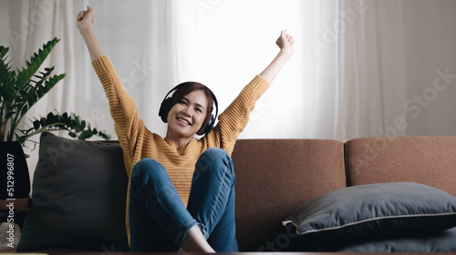 Being energetic. Pretty overjoyed young  woman laughing and listening to music and wearing headphones while sit on the sofa and wearing a yellow sweater