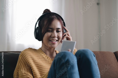Attractive young woman on the sofa at home, she is playing music with her smarphone and wearing headphones, leisure and entertainment concept