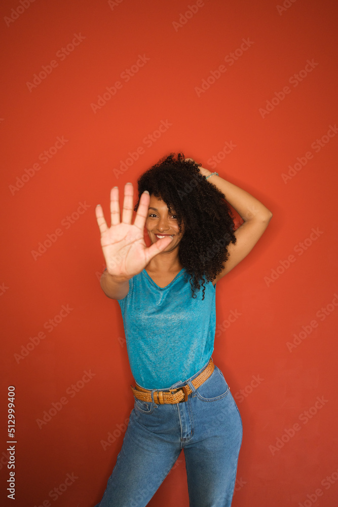 Afro hairstyle cheerful black woman showing hand palm on red wall background. Female doing stop gesture. Afro hairstyle cheerful black woman showing hand palm on red wall background. Female doing stop gesture.