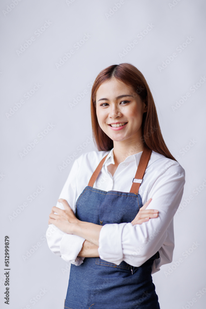 Young Asian woman wearing apron isolated on white background with copy space. Portrait of successful Asian woman with crossed arms on a white wall. Smiling young waitress looking at camera. Young Asian woman wearing apron isolated on white background with copy space. Portrait of successful Asian woman with crossed arms on a white wall. Smiling young waitress looking at camera.