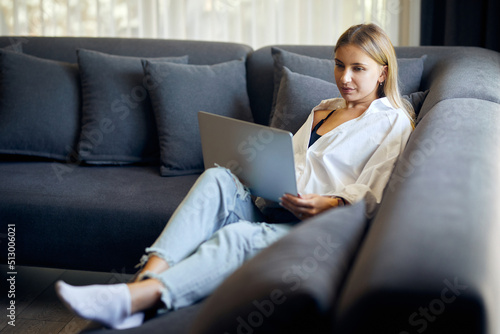 Free Download A woman is sitting on the grey couch and using a laptop for a work - GFXLoad
