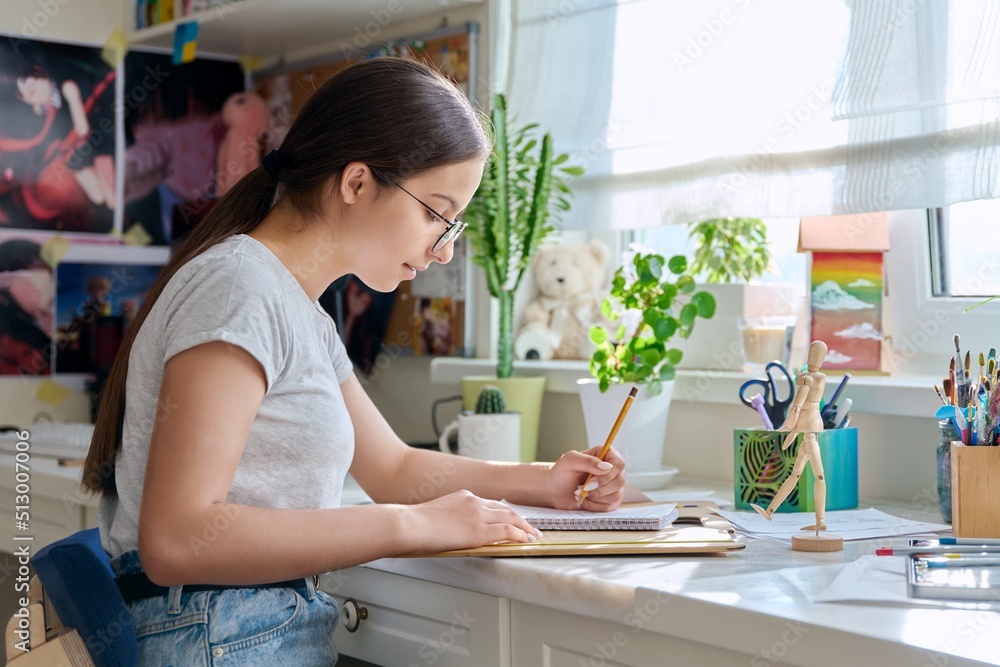 Teenage creative girl artist drawing with a pencil, sitting at the table at home Teenage creative girl artist drawing with a pencil, sitting at the table at home