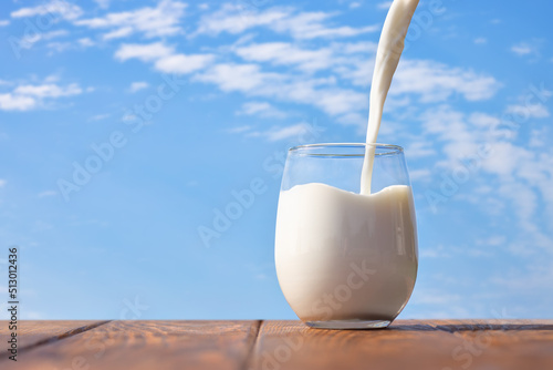 milk pouring into glass on table with blue sky and clouds