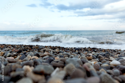 Seascape. Blue and gray pebbles on the beach. White sea waves. Skyline. Nature multicolored background.