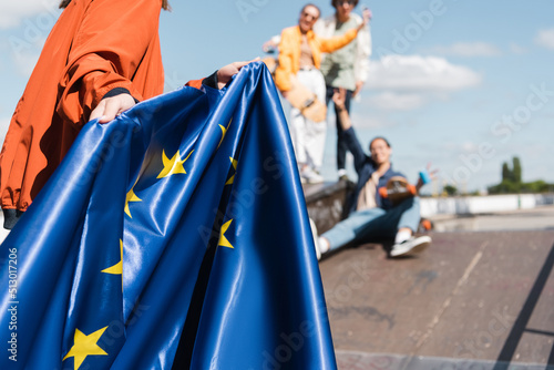 partial view of woman with flag of european union near blurred friends outdoors.