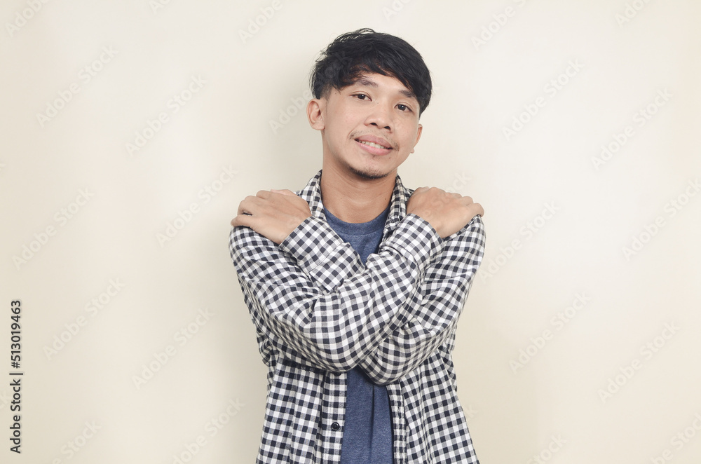 Close-up portrait of happy young Asian male model wearing plaid shirt with self hugging gesture Close-up portrait of happy young Asian male model wearing plaid shirt with self hugging gesture