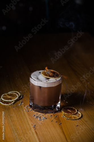 A glass with an alcoholic cocktail in a restaurant bar. Chocolate cocktail decorated with lavender, which is set on fire.
