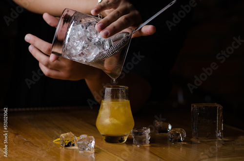 Professional bartender prepares a cocktail with ice at the bar counter. Yellow alcoholic cocktail with the addition of kandurin photo