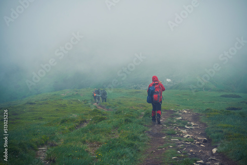 A group of tourists are walking along a mountainous, foggy path. Bad weather in the Carpathian mountains