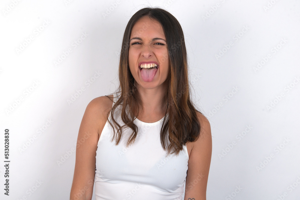 young beautiful caucasian woman wearing white top over white background with happy and funny face smiling and showing tongue. young beautiful caucasian woman wearing white top over white background with happy and funny face smiling and showing tongue.
