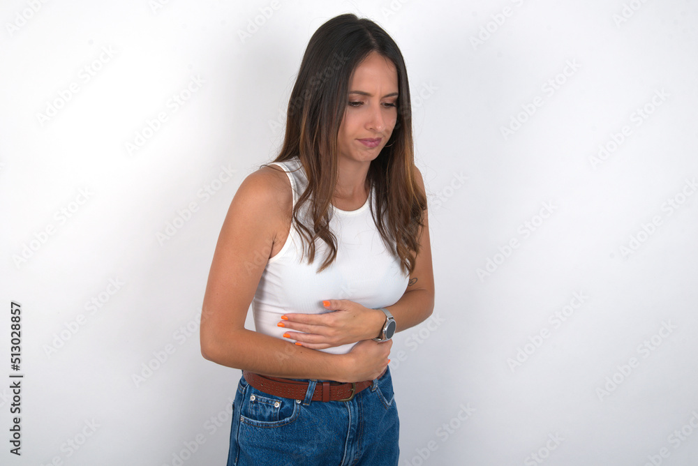 young beautiful caucasian woman wearing white top over white background suffering from strong stomachache. young beautiful caucasian woman wearing white top over white background suffering from strong stomachache.