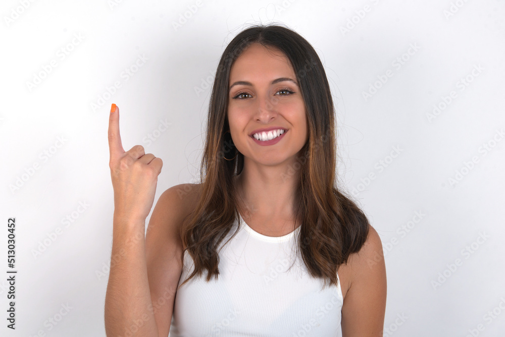 young beautiful caucasian woman wearing white Top over white background smiling and looking friendly, showing number one or first with hand forward, counting down young beautiful caucasian woman wearing white Top over white background smiling and looking friendly, showing number one or first with hand forward, counting down