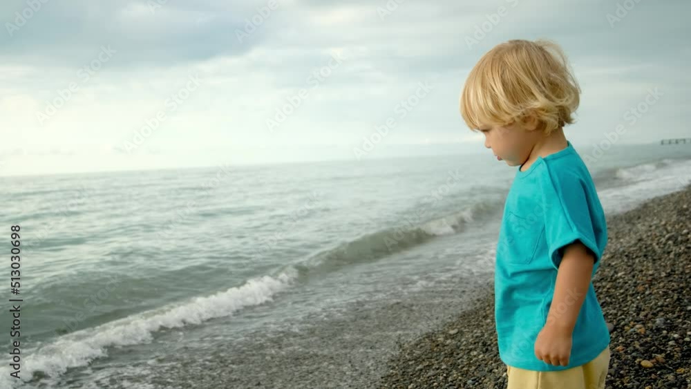 A little boy is playing on the seashore, he throws stones into the water. Family vacation by the sea. A little boy is playing on the seashore, he throws stones into the water. Family vacation by the sea.