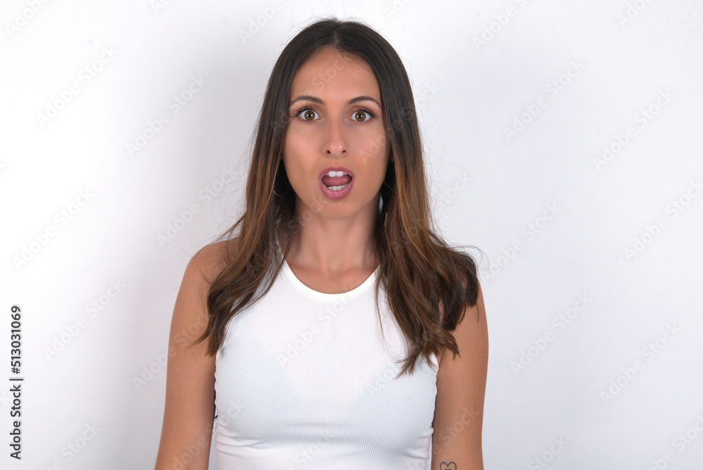 Shocked young beautiful caucasian woman wearing white Top over white background, stares bugged eyes keeps mouth opened has surprised expression. Omg concept Shocked young beautiful caucasian woman wearing white Top over white background, stares bugged eyes keeps mouth opened has surprised expression. Omg concept