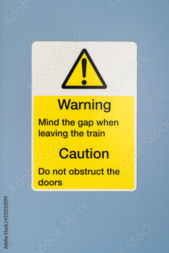 Generic yellow, black and white train door and gap warning sticker on a light blue surface.