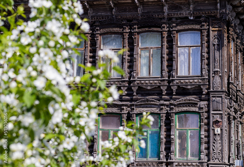 Carved wooden trim facade. Old historic house. Russian architecture. Chopped house with carved wooden architraves. Apple blossom. Tomsk, Russia