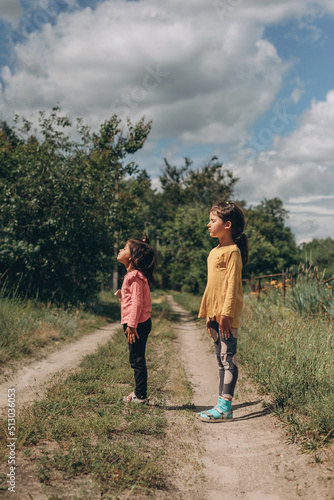 Two little girls with closed eyes raised their heads up to the sky with faith and hope for a better future, Ukrainian children