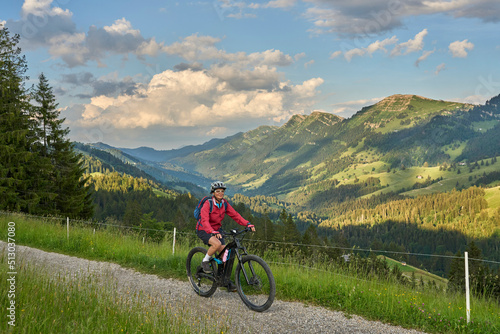 pretty senior woman riding her electric mountain bike on the mountains above Oberstaufen with Nagelfluh mountain chain in background, Allgau Alps, Bavaria Germany 